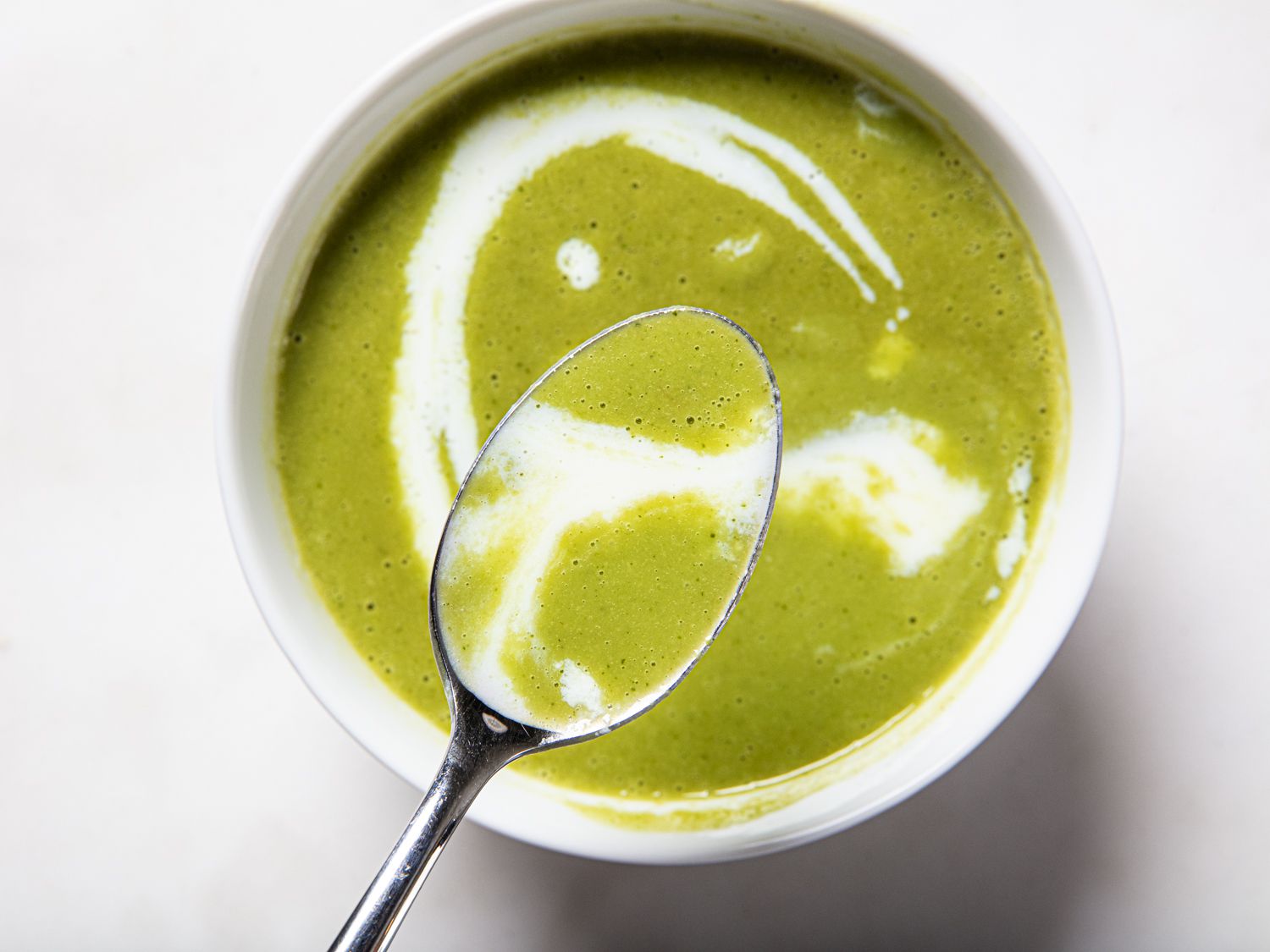 A spoon of garlic scape soup topped with cream lifted over the bowl