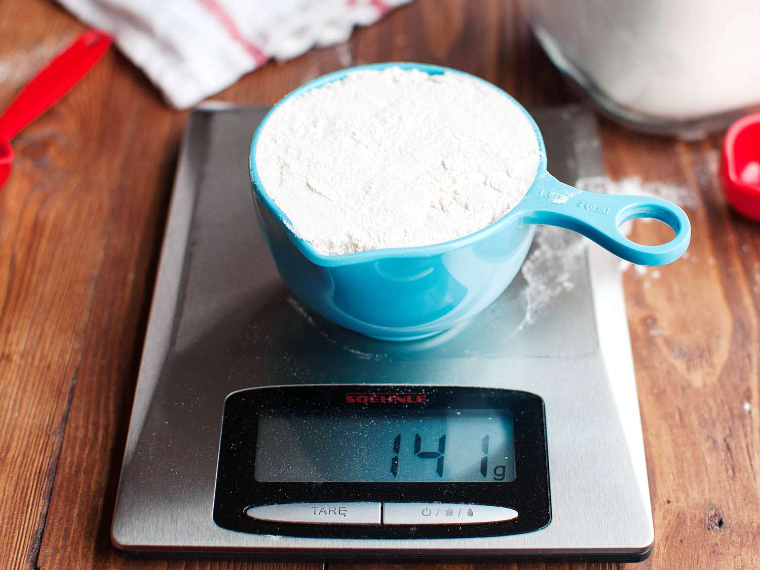 The cup of flour is measured on a tared scale at 141 grams.