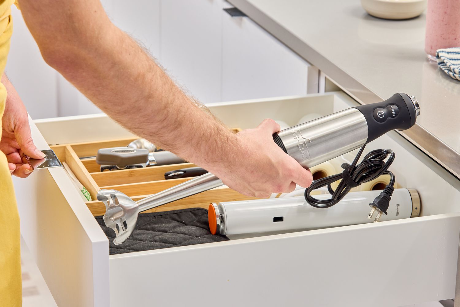 A person tucks the All-Clad Stainless Steel Immersion Blender inside a kitchen drawer