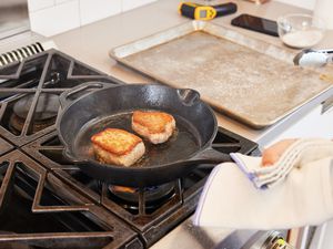 A person searing pork in a cast iron skillet.