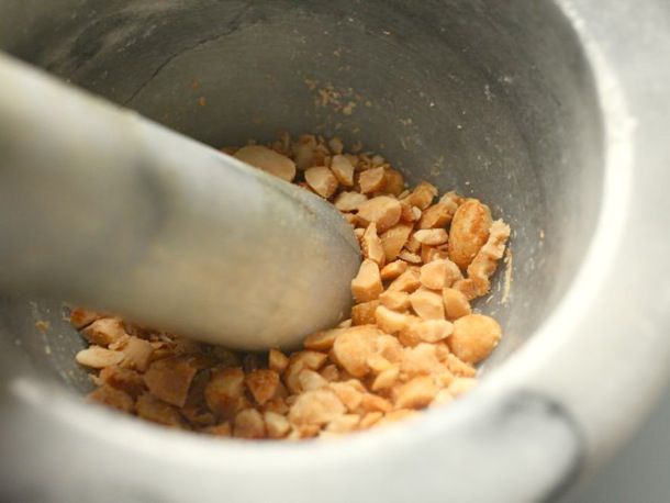 Grinding roasted peanuts with mortar and pestle.