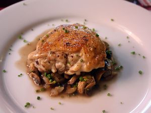 Crusty chicken with mushrooms and white wine on a plate, sprinkled with chopped fresh herbs. 
