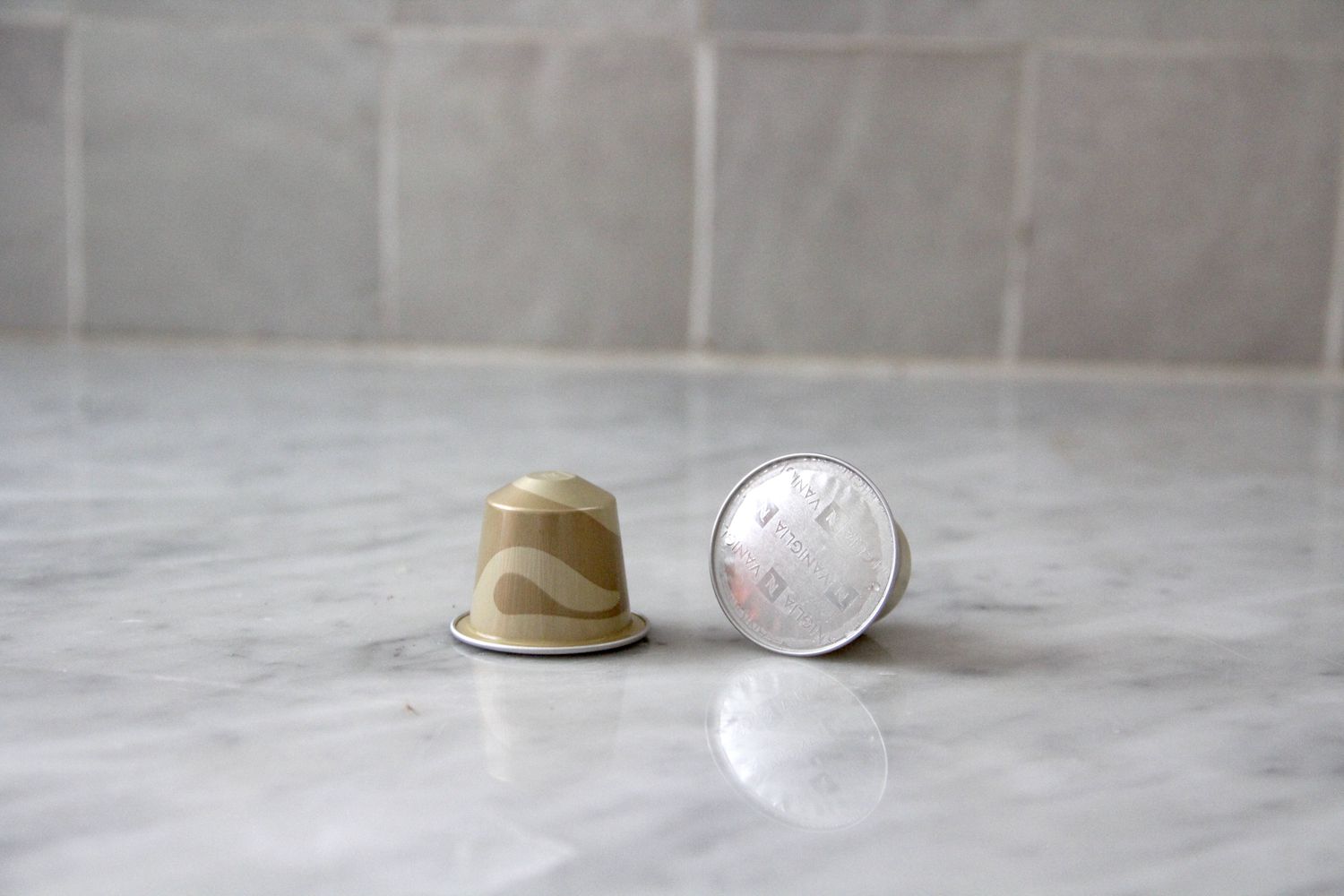 Two vanilla Nespresso pods on a marble kitchen countertop.