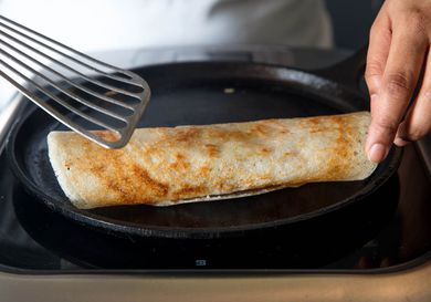 Rolling a cooked dosa on a cast iron griddle