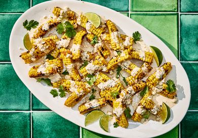 Bright colorful photo of grilled corn, topped with sauce, cheese cilantro and limes. 