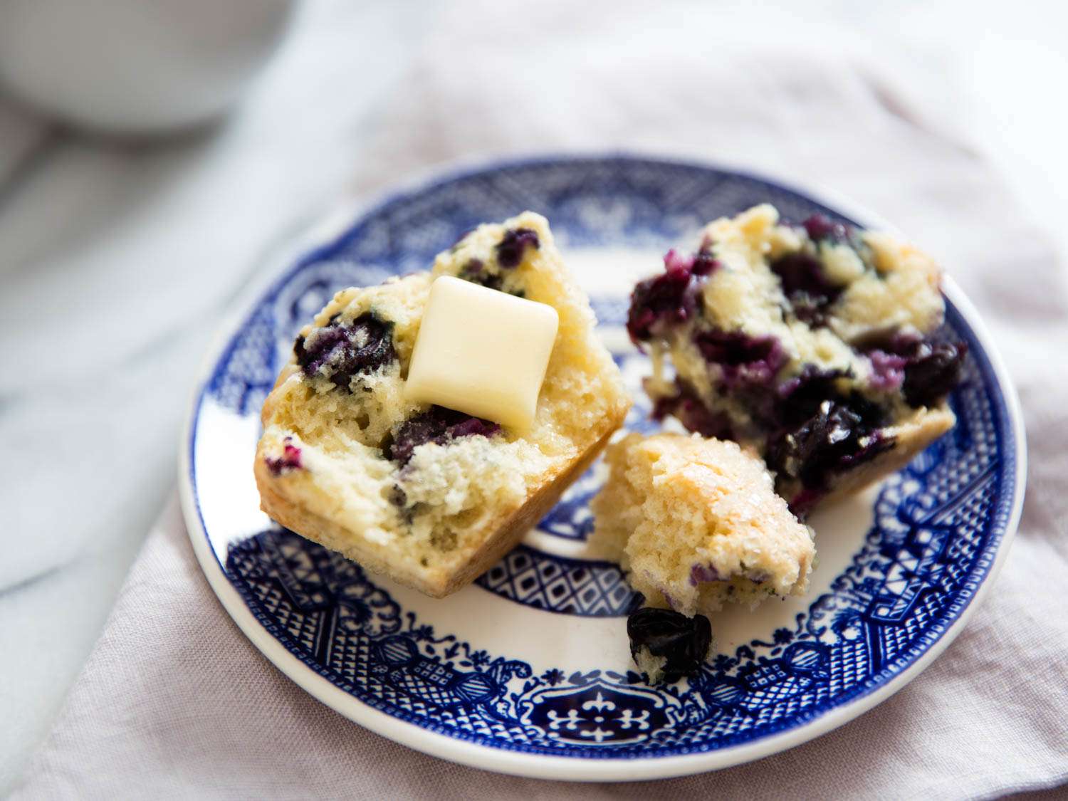A split blueberry muffin topped with a pat of butter.