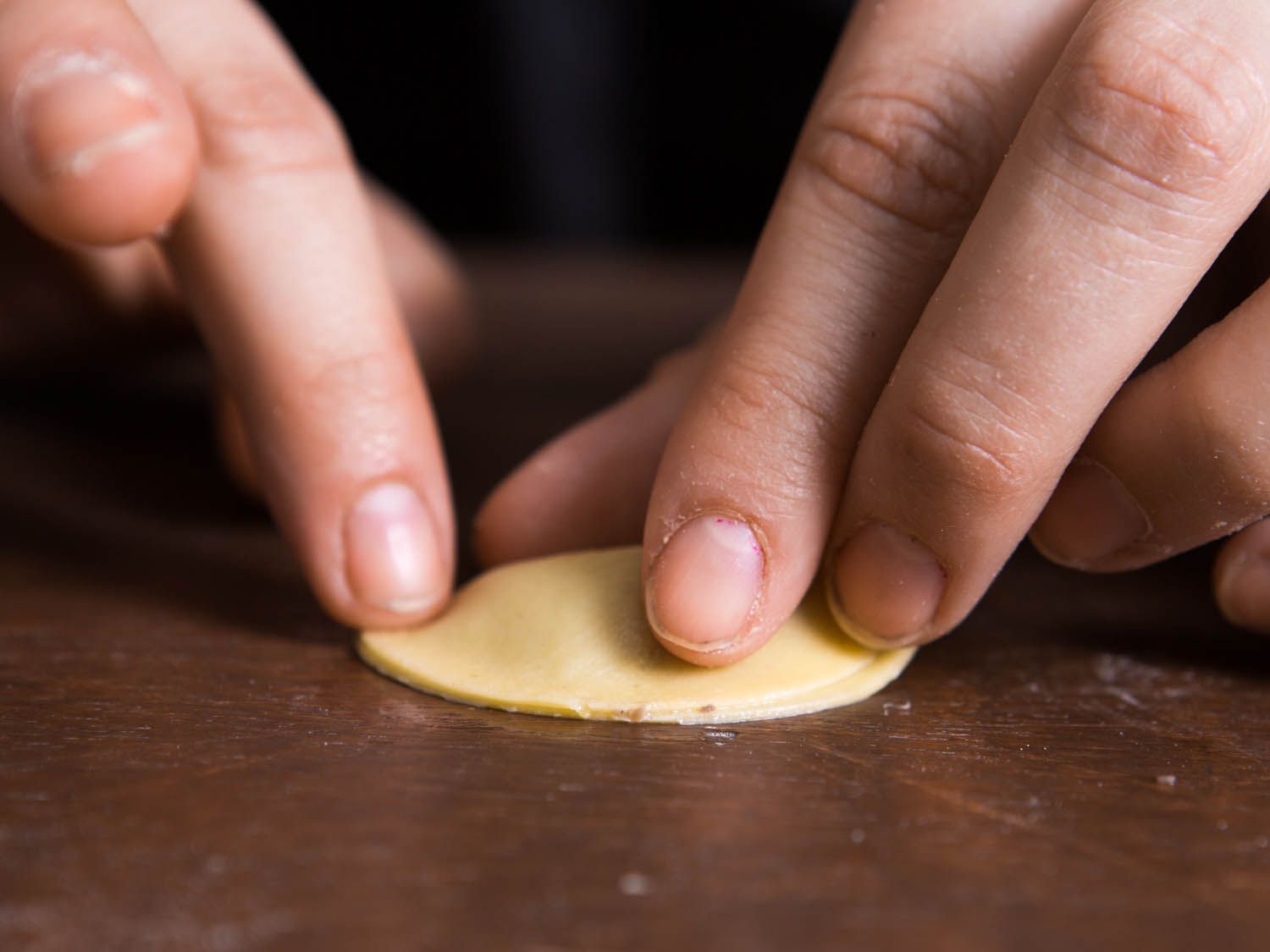 Fingers folding pasta dough over filling to make a tortellini (or mezzaluna if left as is).