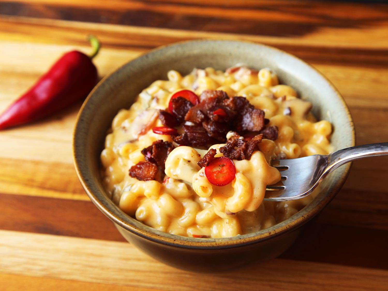 A bite of bacon-jalapeño mac and cheese is lifted toward the camera on a fork.