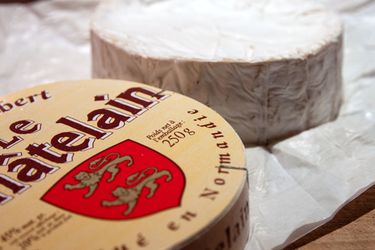 A wheel of camembert next to it's wooden packaging.