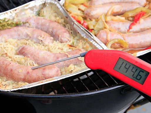 An instant-read thermometer stuck in a pan of sausages on the grill