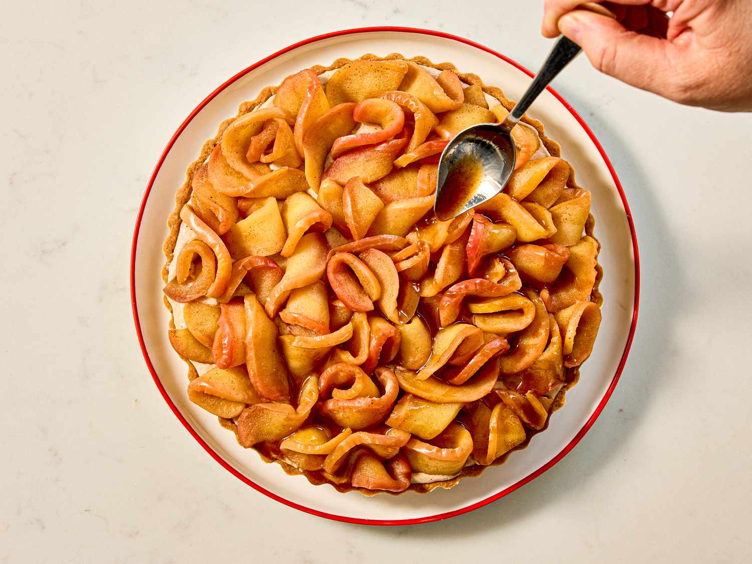 A caramel apple tart on a plate with a spoon adding topping