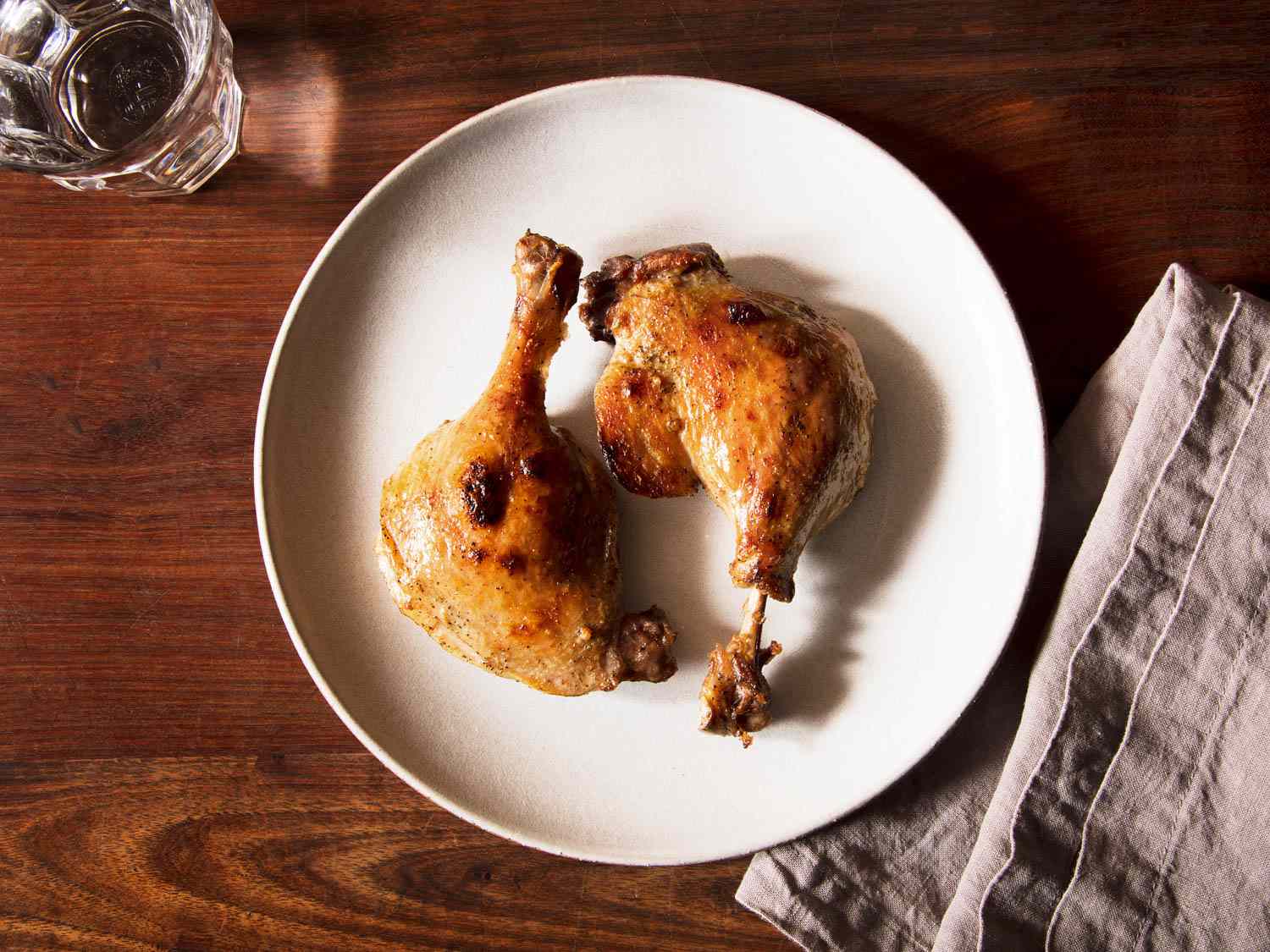 An overhead view of two pieces of duck on a white platter on a wooden table.