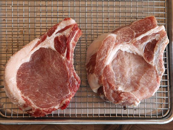 Two pork chops resting on a wire rack, one un-brined and one brined