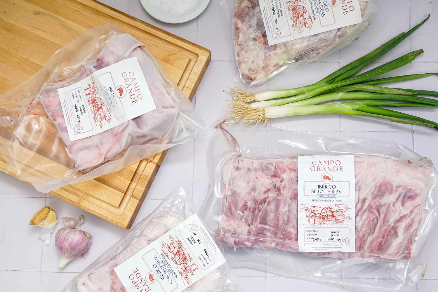 Packaged ibrico pork ribs on a cutting board surrounded by green onions garlic and other food items