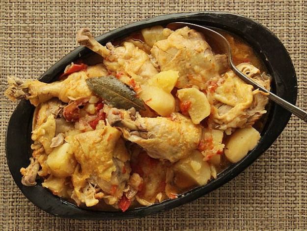 A crock pot insert with Colombian Chicken Stew With Potatoes, Tomato, and Onion and a serving spoon.