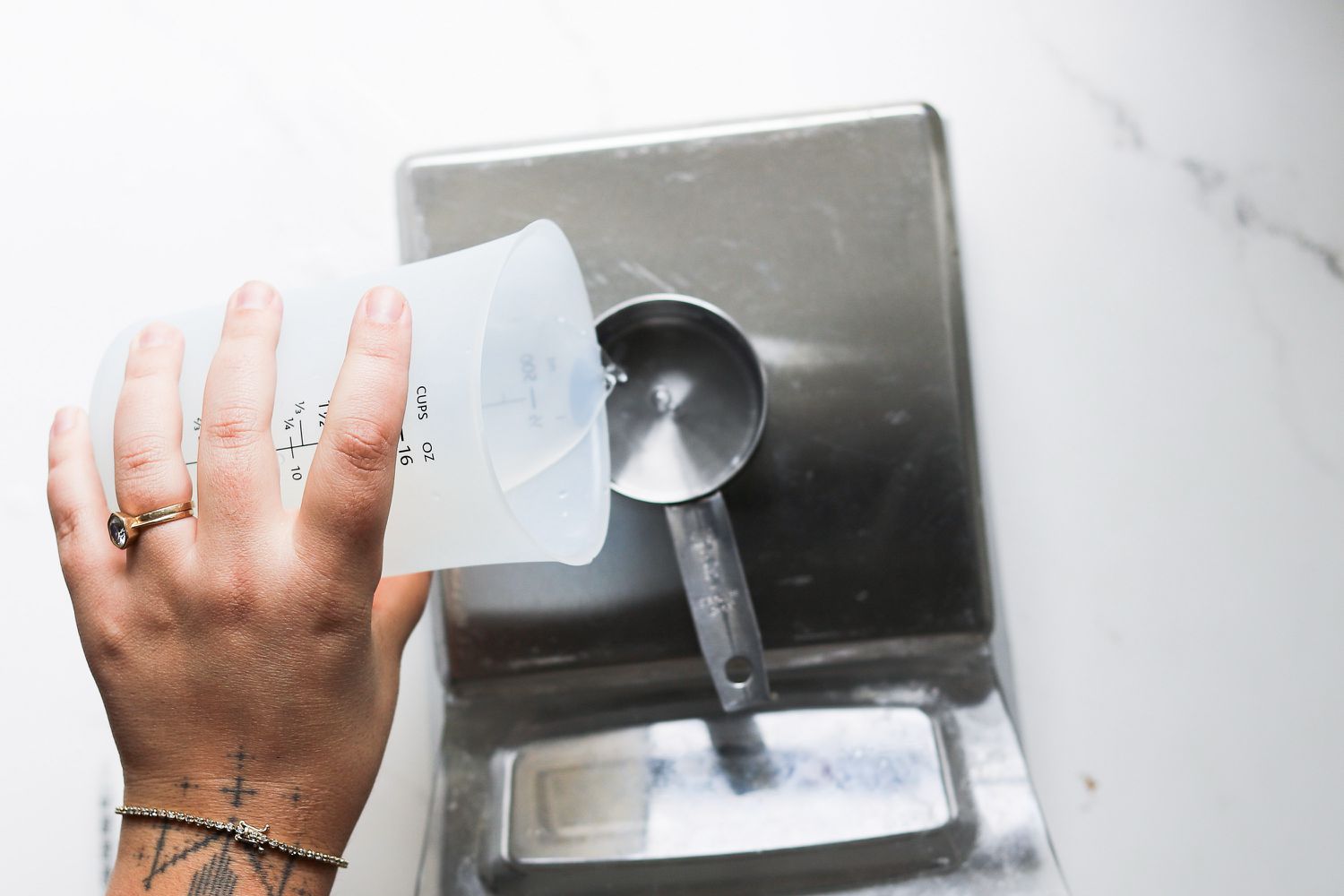 A person pouring water into a measuring cup set on a scale.
