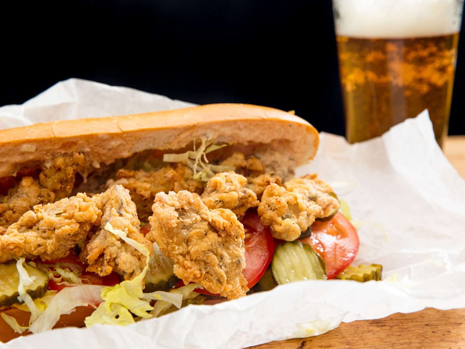 Closeup of oyster po' boy with beer in background.