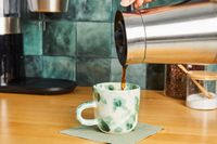 A person pouring coffee into a green and white mug.