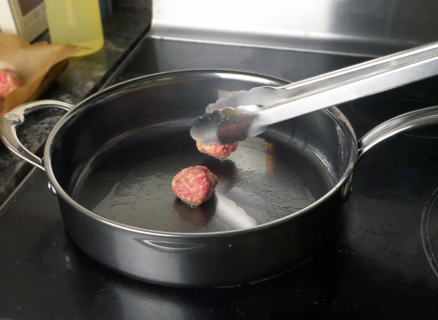 using tongs to add a meatball to a saute pan