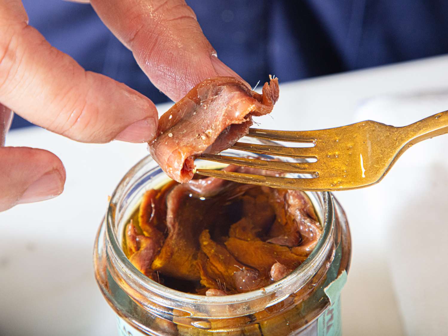 A hand holding anchovies from a jar with a fork