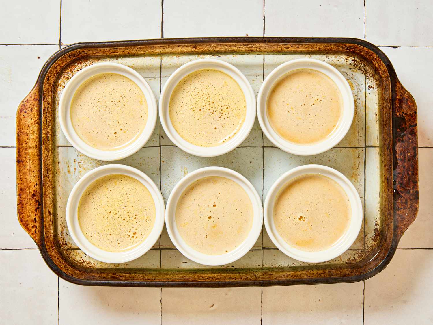 Six ramekins filled with custard in a baking dish