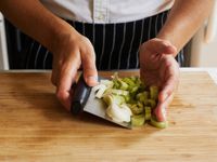 A cook uses a bench scraper to transfer chopped leeks