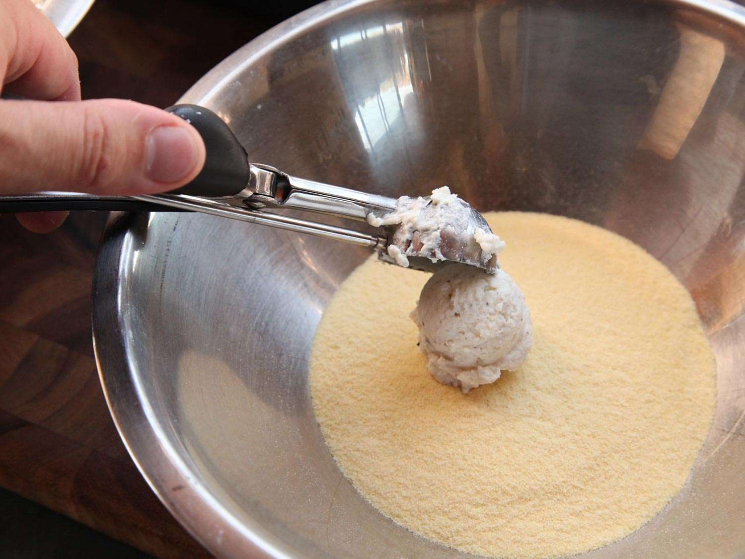 Dropping the ricotta ball into a bowl of semolina flour. 