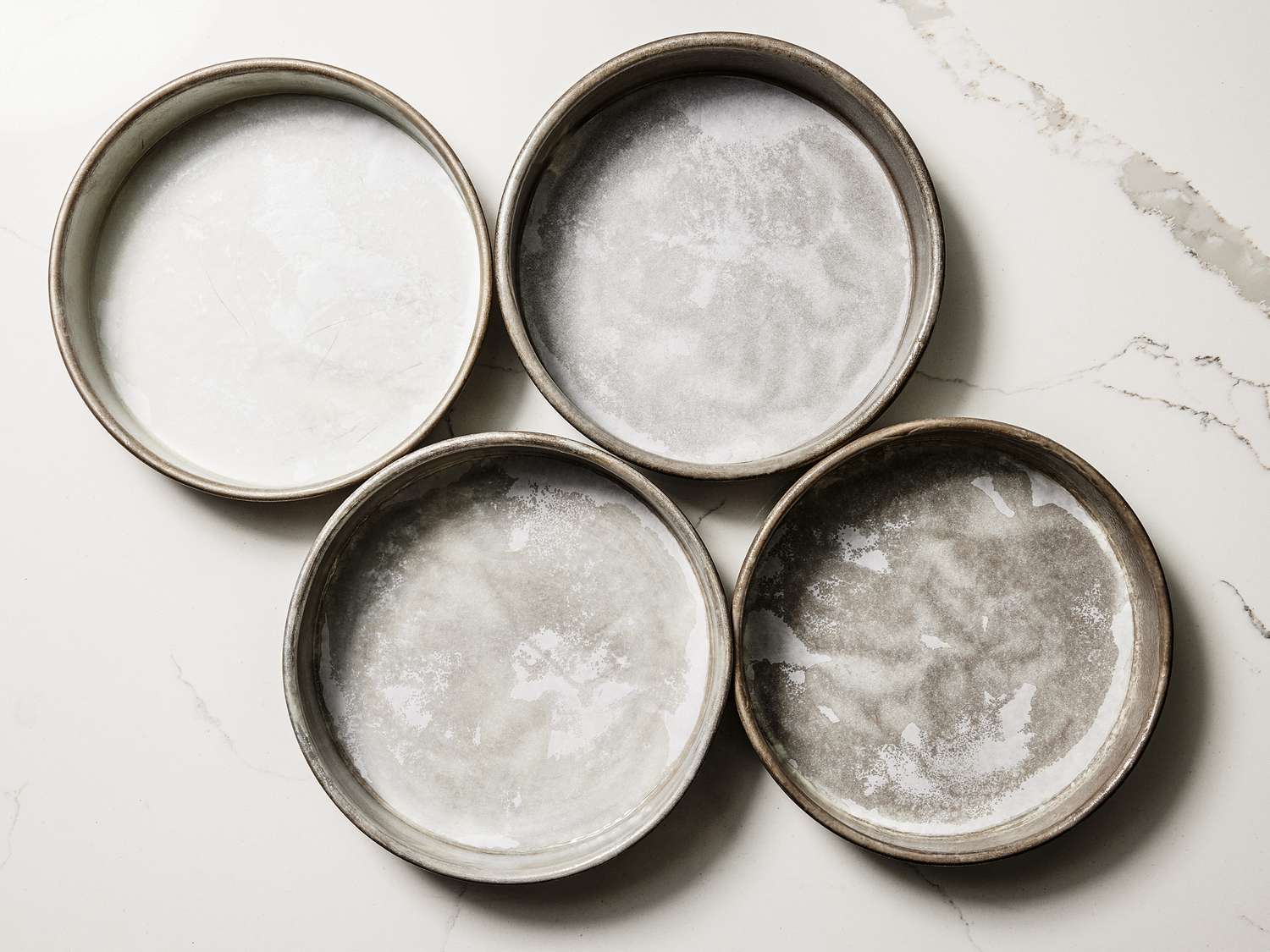 4 prepared cake tins on a white marble surface 