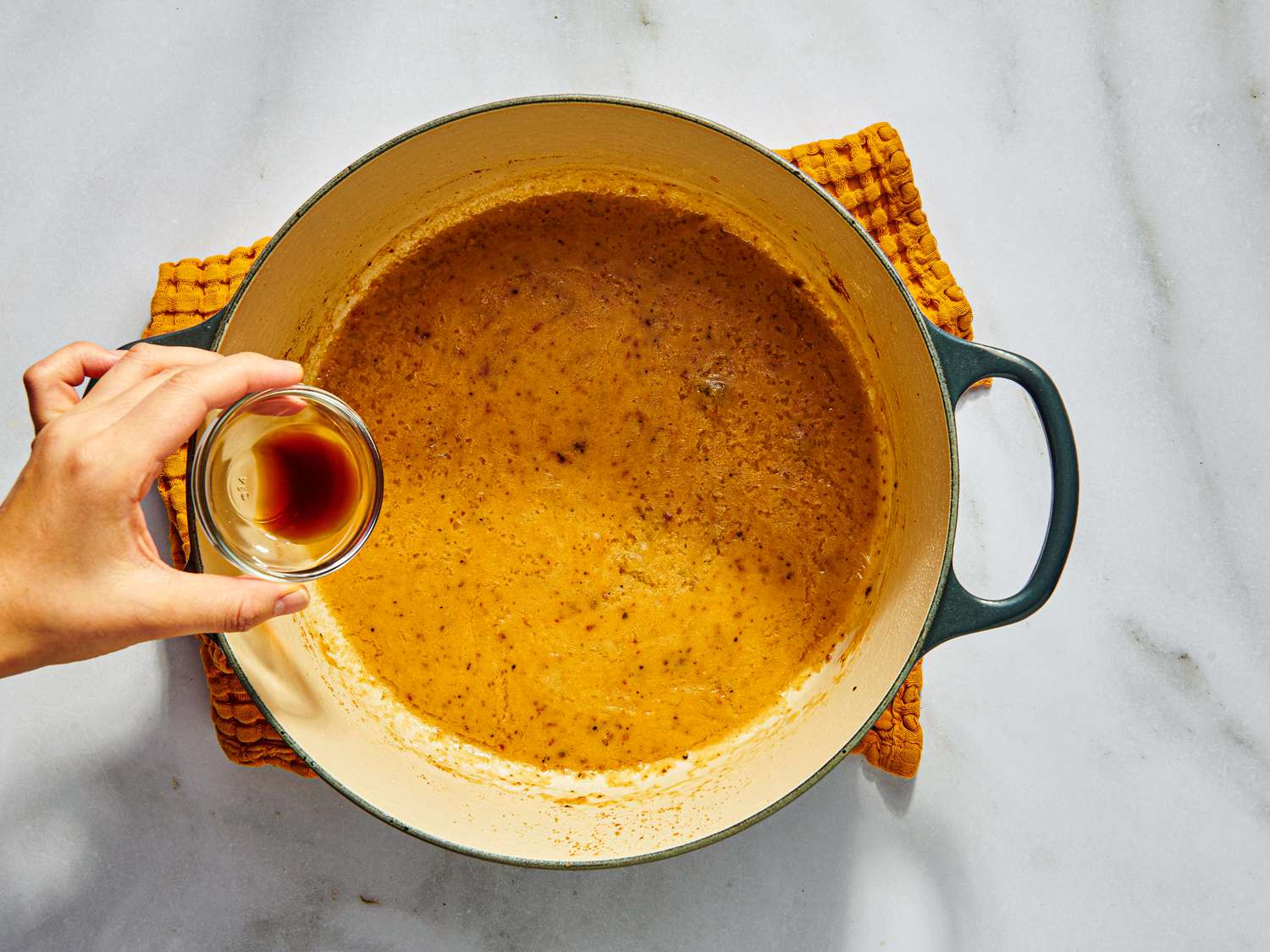 gravy in dutch oven, cooling on towel, with a small ramekin of soy sauce being poured in 