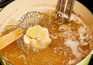 Dipping breaded pickles into heated oil in dutch oven with slotted spoon 