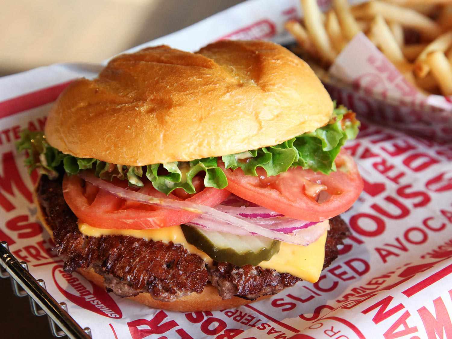 A smashburger with a container of french fries in the background