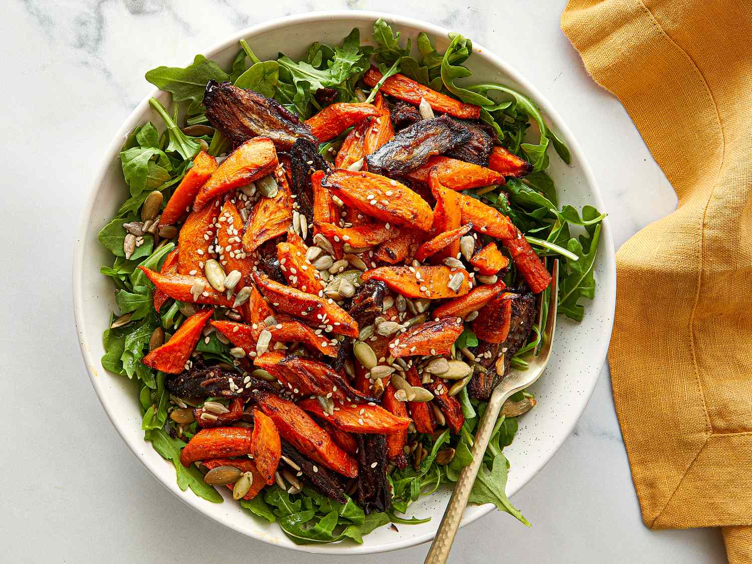Salad with roasted carrots dates seeds on greens with a fork