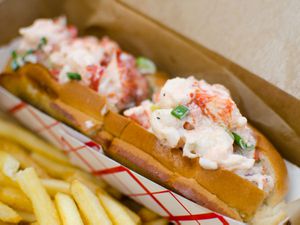Lobster rolls in a basket next to some French fries. 