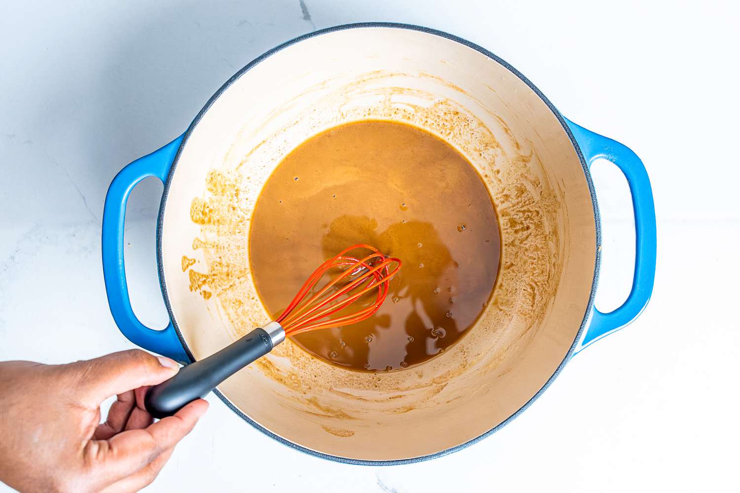 A person uses a silicone whisks to cook roux in a cast iron enameled pot.