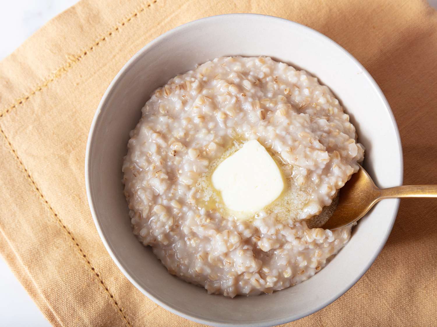 Rice Cooker Oatmeal with butter on top, with a gold spoon and gold napkin