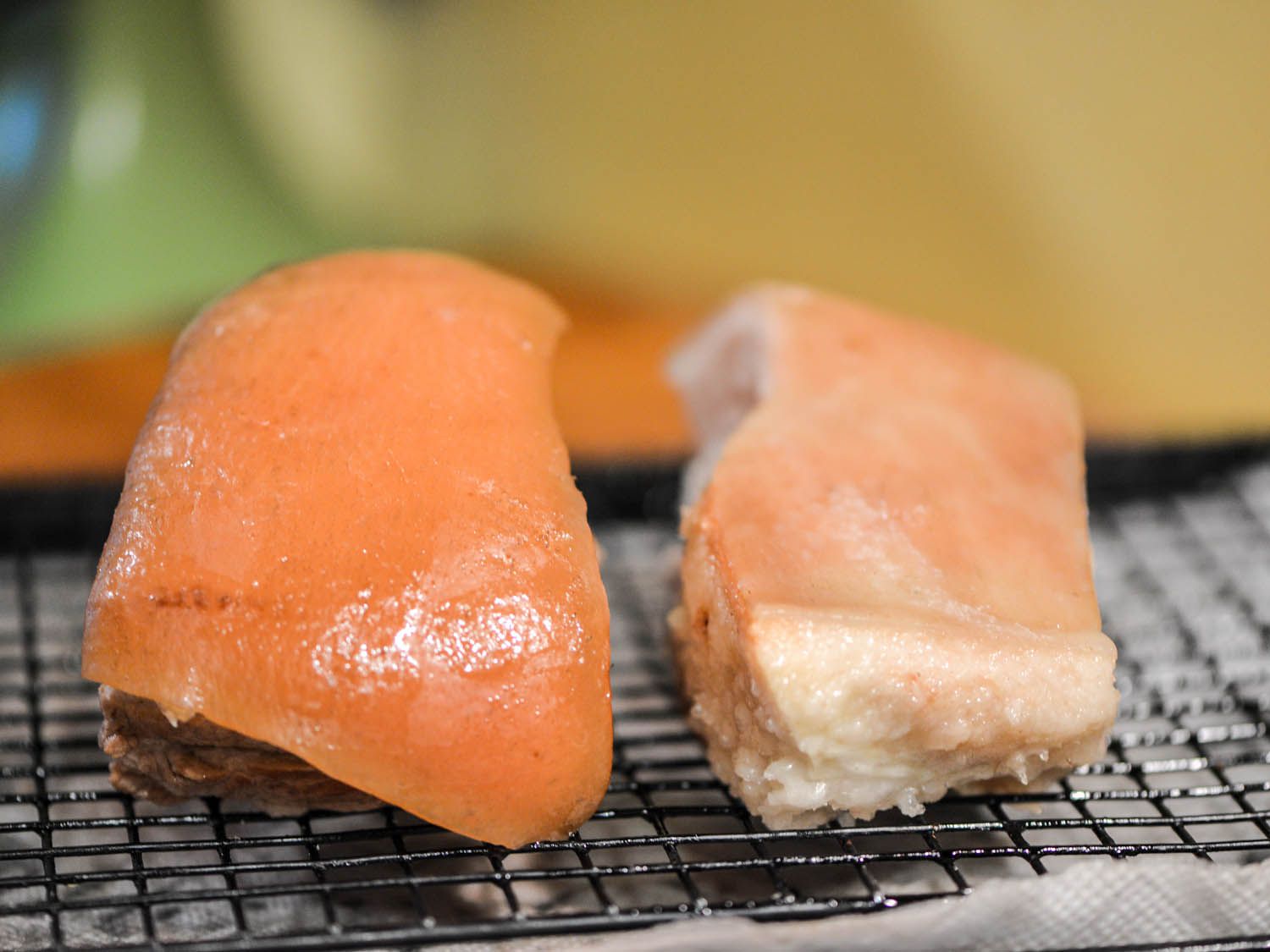 A side-by-side comparison of two pieces of pork belly on a wire rack with the left having been boiled in seasonings and the right having been boiled in salt water.