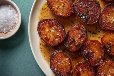 Closeup of a serving platter of fondant potatoes with a ramekin of flaky sea salt on the side.