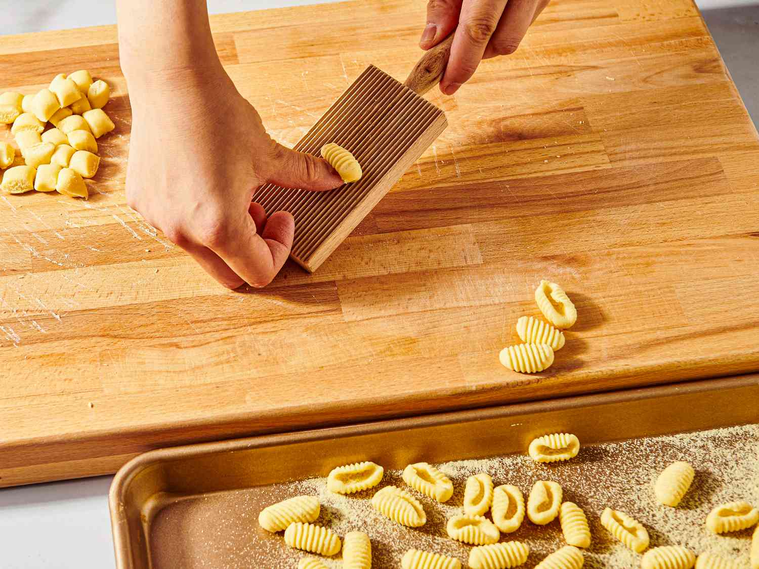 Pressing dough with a gnocchi board, with pressed pastas on a baking sheet