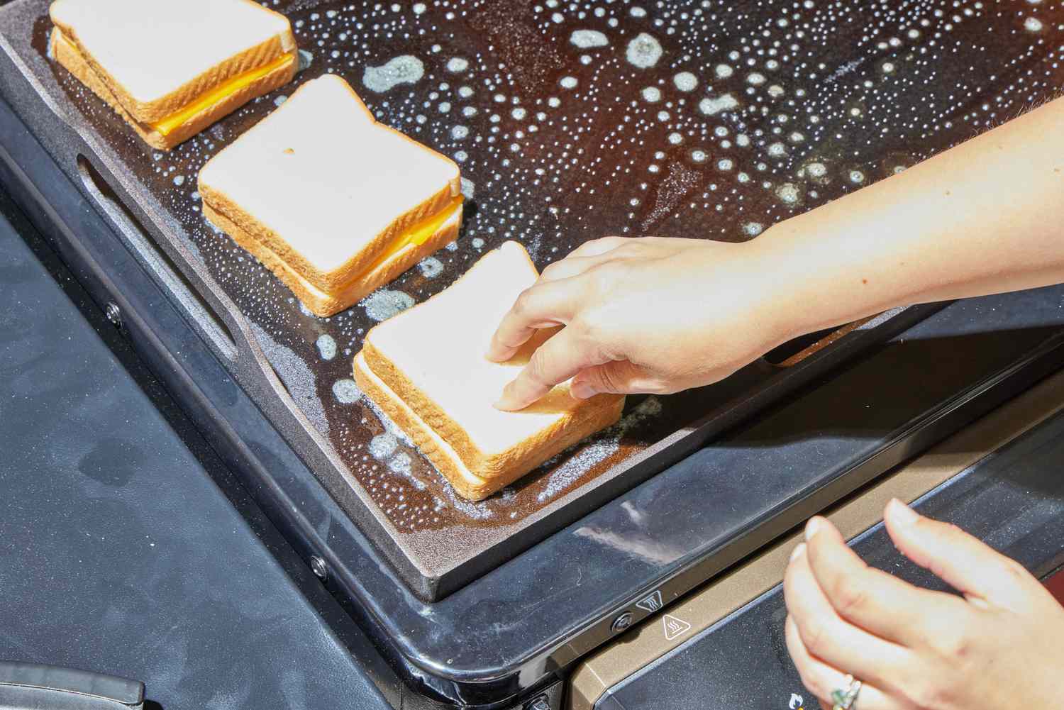 A person cooks grilled cheese on the Traeger Flatrock Flat Top Grill