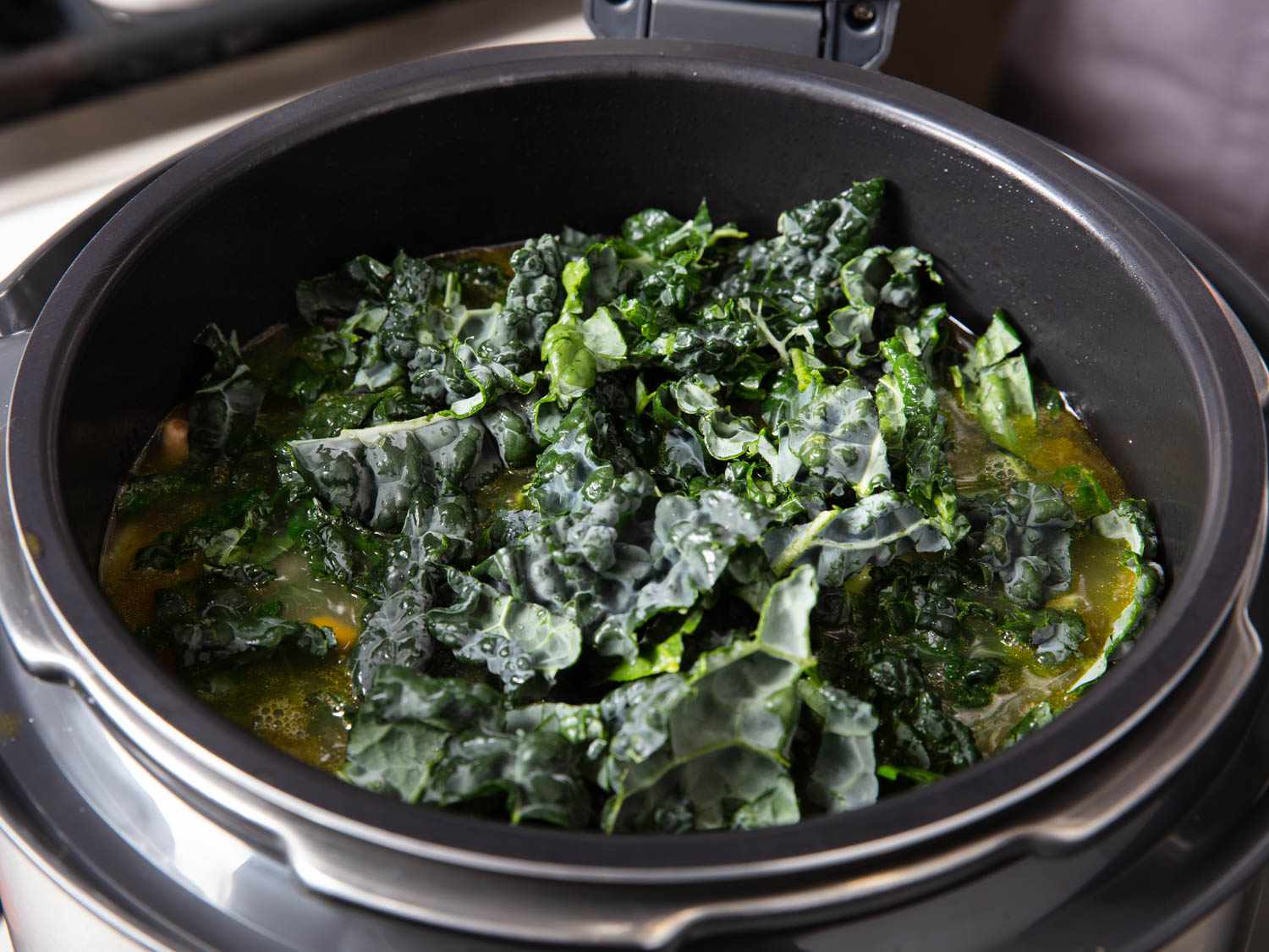 A pile of kale being added to a pressure cooker filled with ribollita