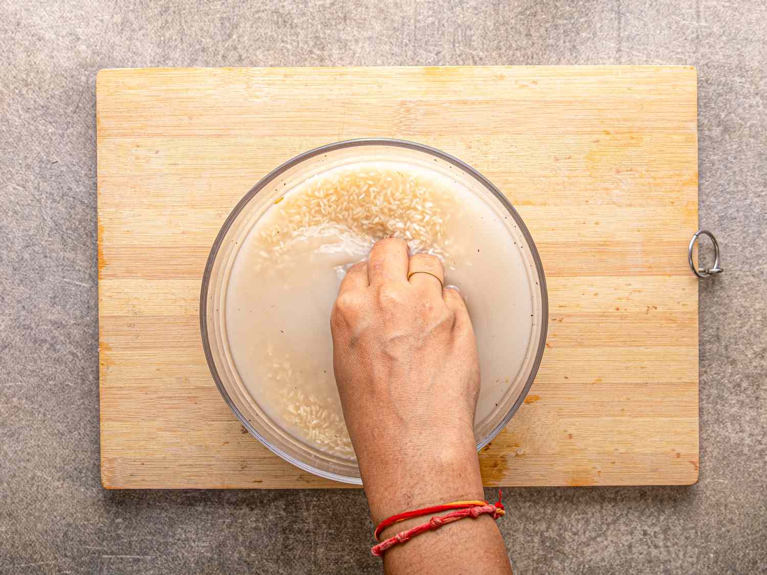 A hand rinsing rice in a bowl on a cutting board