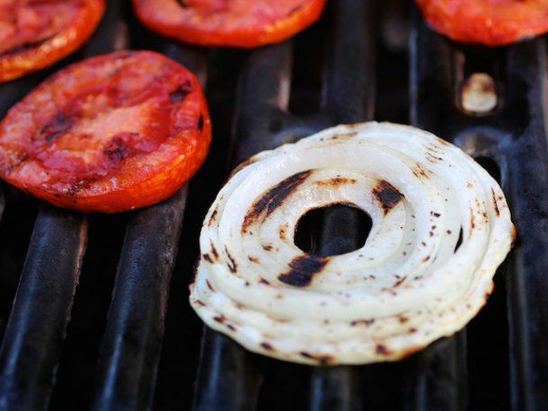 Sliced onion and tomato getting nicely charred on a grill grate.