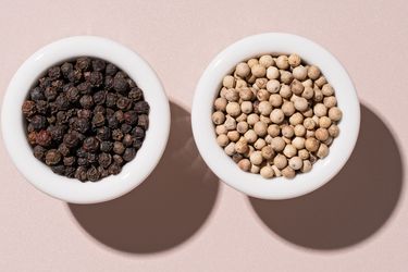 Bowl of black peppercorns and a bowl of white peppercorns