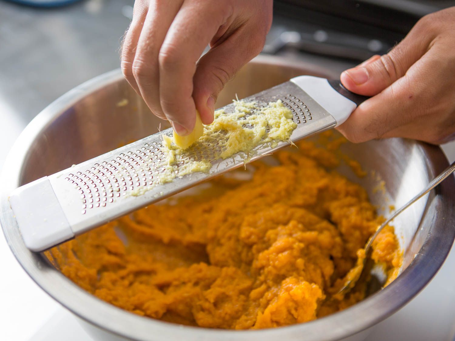 Grating fresh ginger over mashed sweet potatoes with microplane