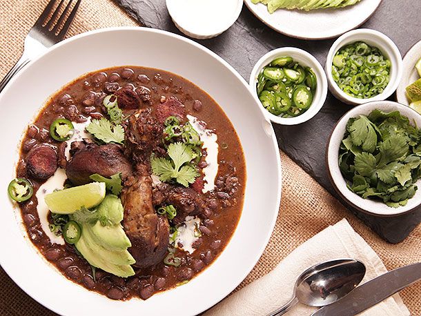 Bowl of black bean soup with large pieces of meat, avocados, and jalapenos on top. 