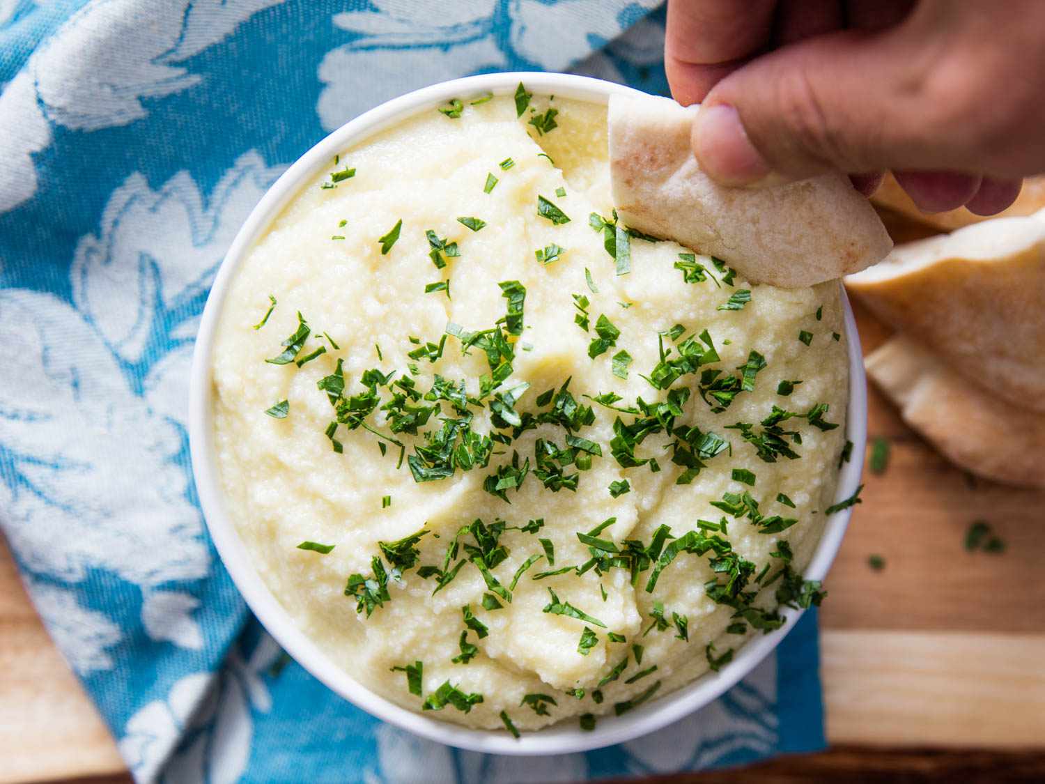 Overhead shot of pita being dipped into small white bowl of potato puree.