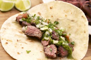 Sliced marinated grilled flank steak nestled in a flour tortilla with topped with green salsa 