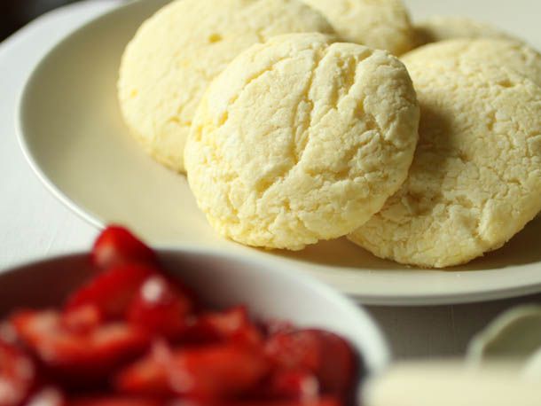 Closeup of gluten free short cakes on a plate. A bowl of strawberries is in the foreground, blurred by the narrow depth of field.