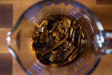 Overhead of dried mushrooms soaking in stock in a glass measuring cup.