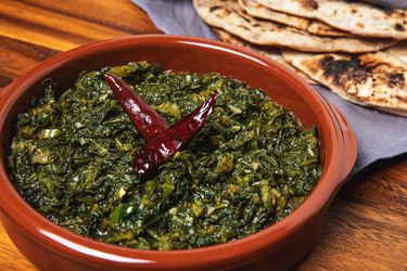 Saag in an earth-toned orange bowl with roti in the background